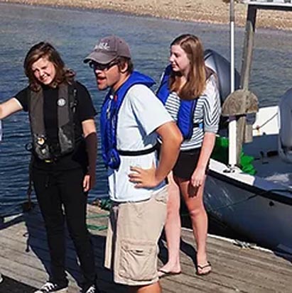 Three people in life vests standing on a dock.