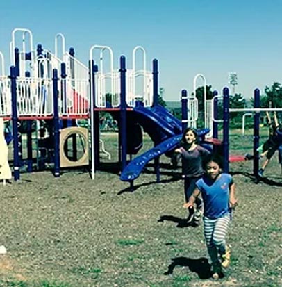 Kid running in front of a playground set. 